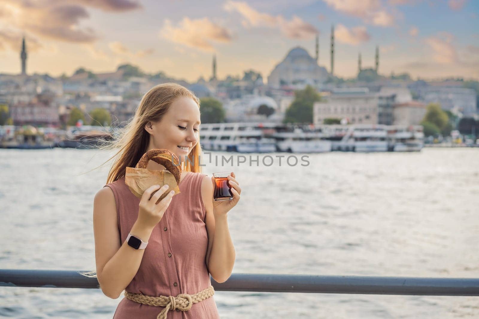 Woman in Istanbul having breakfast with Simit and a glass of Turkish tea. Glass of Turkish tea and bagel Simit against golden horn bay in Istanbul, Turkey. Turkiye.