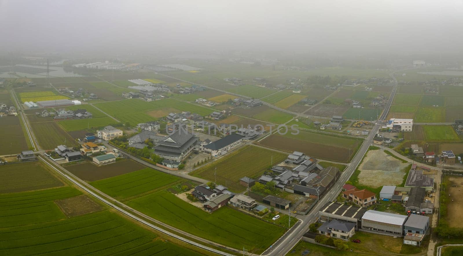 Aerial view of buildings and roads under low fog in Japanese countryside. High quality photo