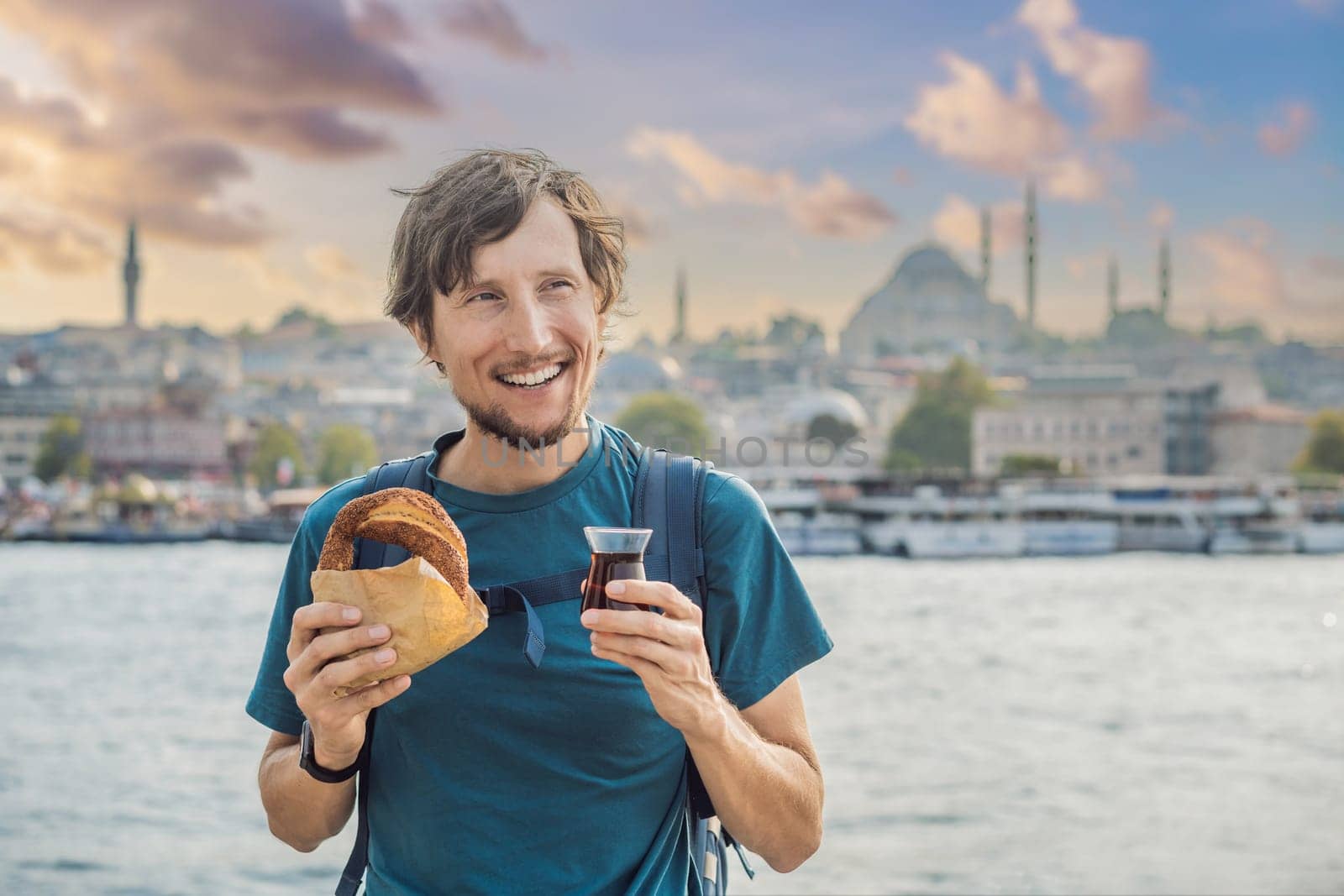 Man in Istanbul having breakfast with Simit and a glass of Turkish tea. Glass of Turkish tea and bagel Simit against golden horn bay in Istanbul, Turkey. Turkiye.