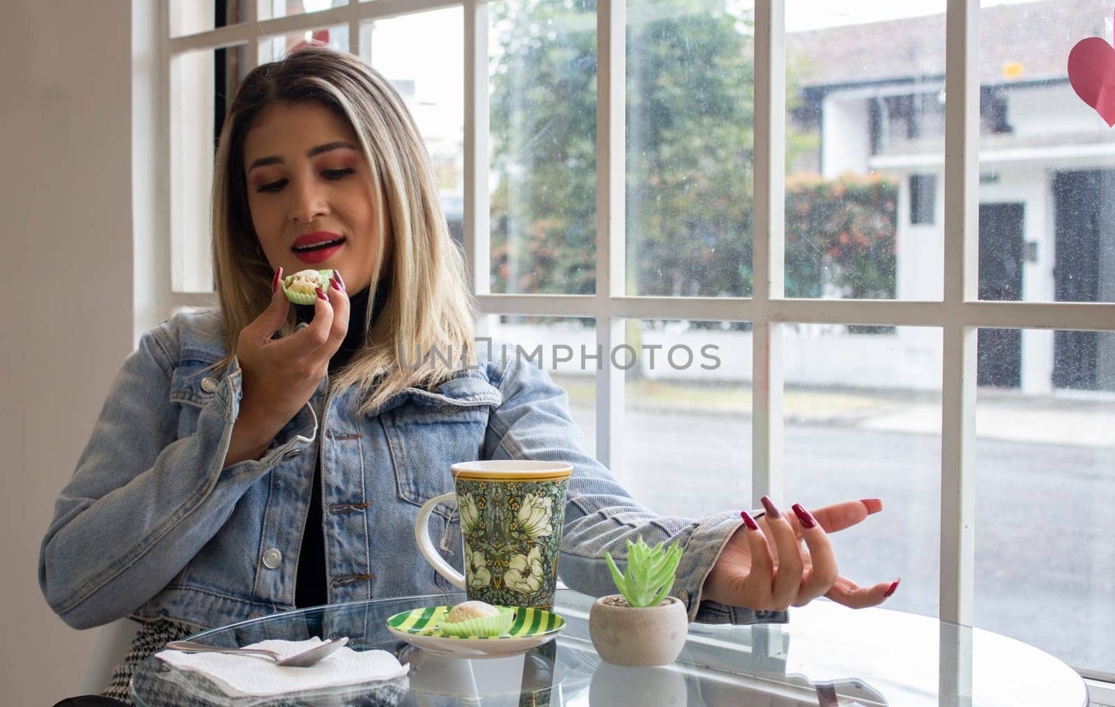 blonde woman eating a cake and having a coffee by the window of a cafeteria. High quality photo