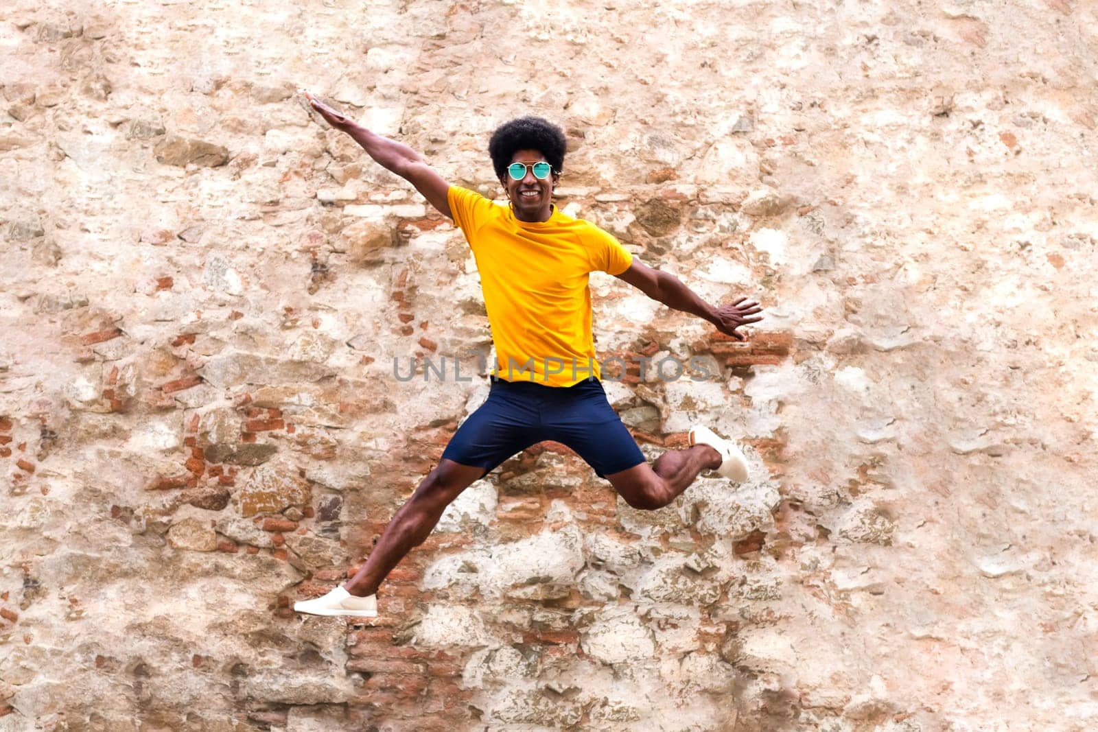 Happy young African American man jumping in the air. Rustic brick and stone wall background. Happiness concept.