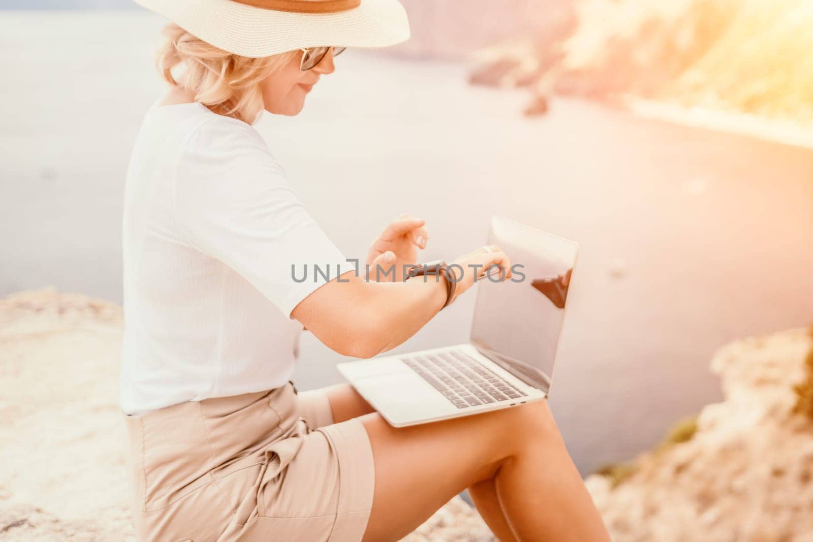 Digital nomad, Business woman working on laptop by the sea. Pretty lady typing on computer by the sea at sunset, makes a business transaction online from a distance. Freelance remote work on vacation