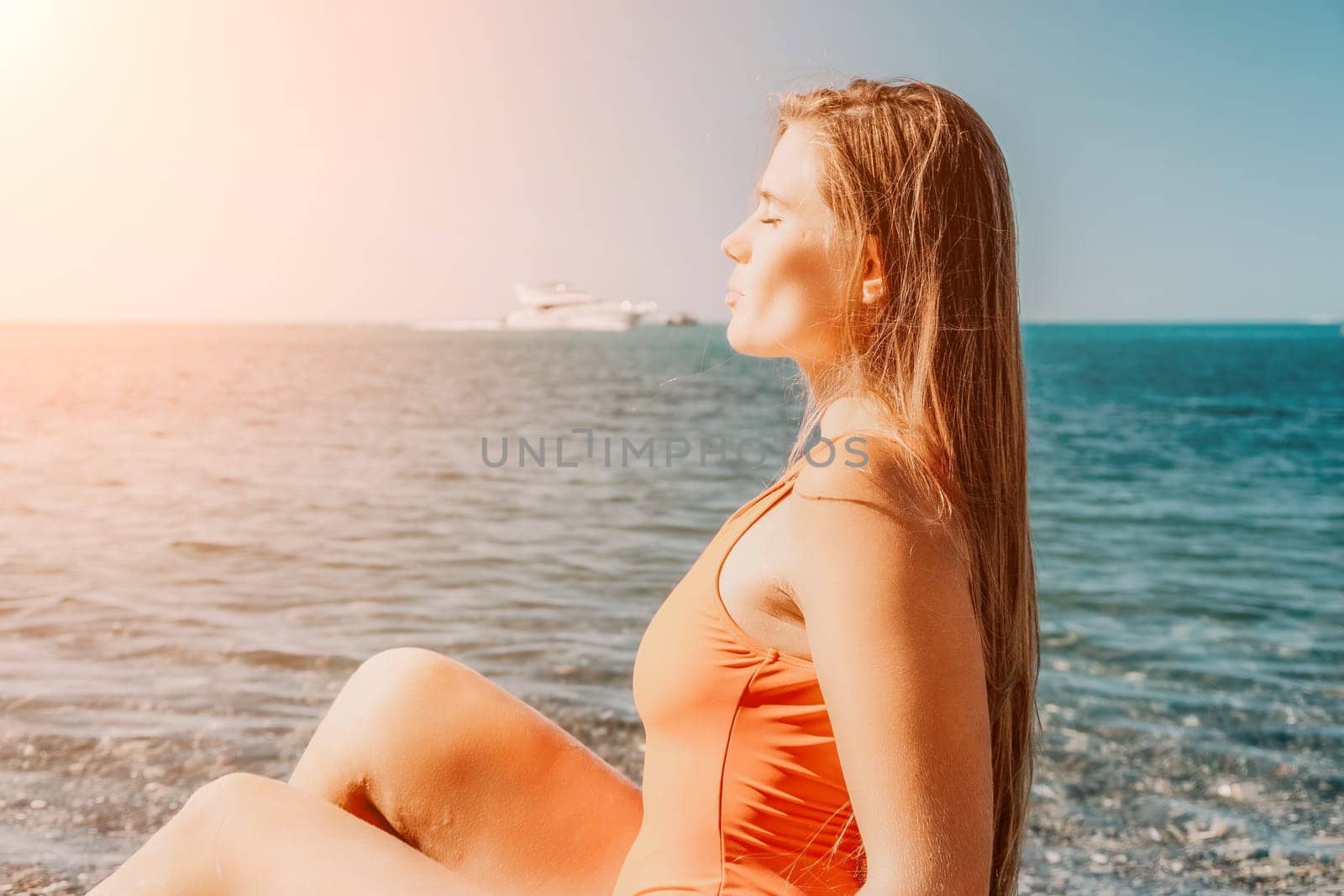 Young woman in red bikini on Beach. Girl lying on pebble beach and enjoying sun. Happy lady with long hair in bathing suit chilling and sunbathing by turquoise sea ocean on hot summer day. Close up by panophotograph