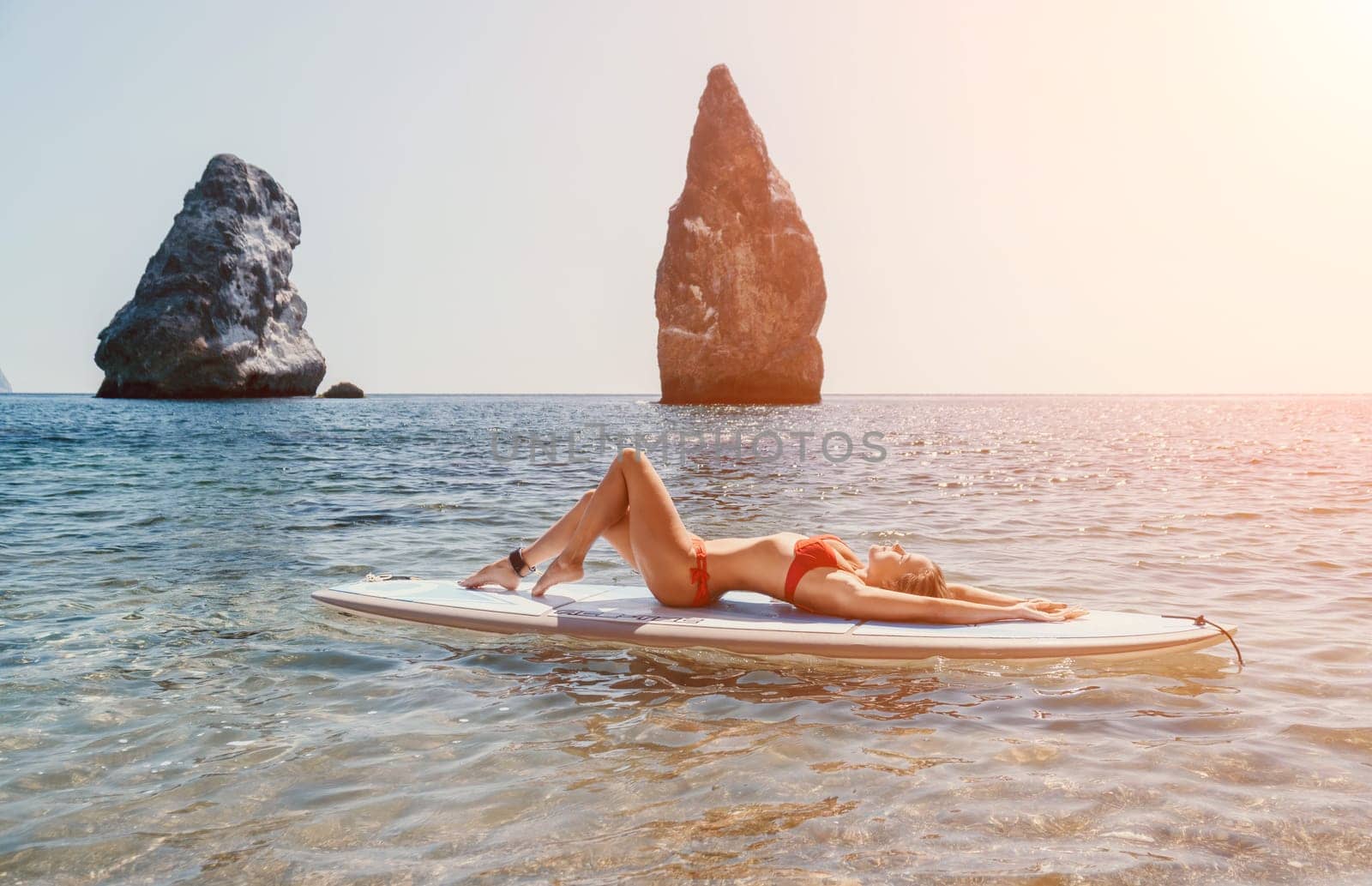 Woman sea sup. Close up portrait of happy young caucasian woman with blond hair looking at camera and smiling. Cute woman portrait in red bikini posing on sup board in the sea by panophotograph