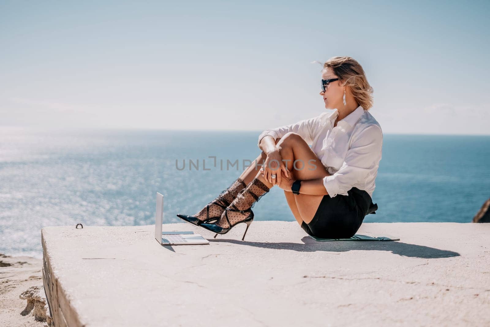 Woman sea laptop. Business woman in yellow hat freelancer with laptop working over blue sea beach. Girl relieves stress from work. Freelance, digital nomad, travel and holidays concept by panophotograph