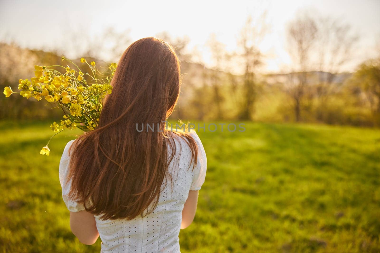 photo from the back of a red-haired woman with a bouquet of flowers in the rays of the setting sun. High quality photo