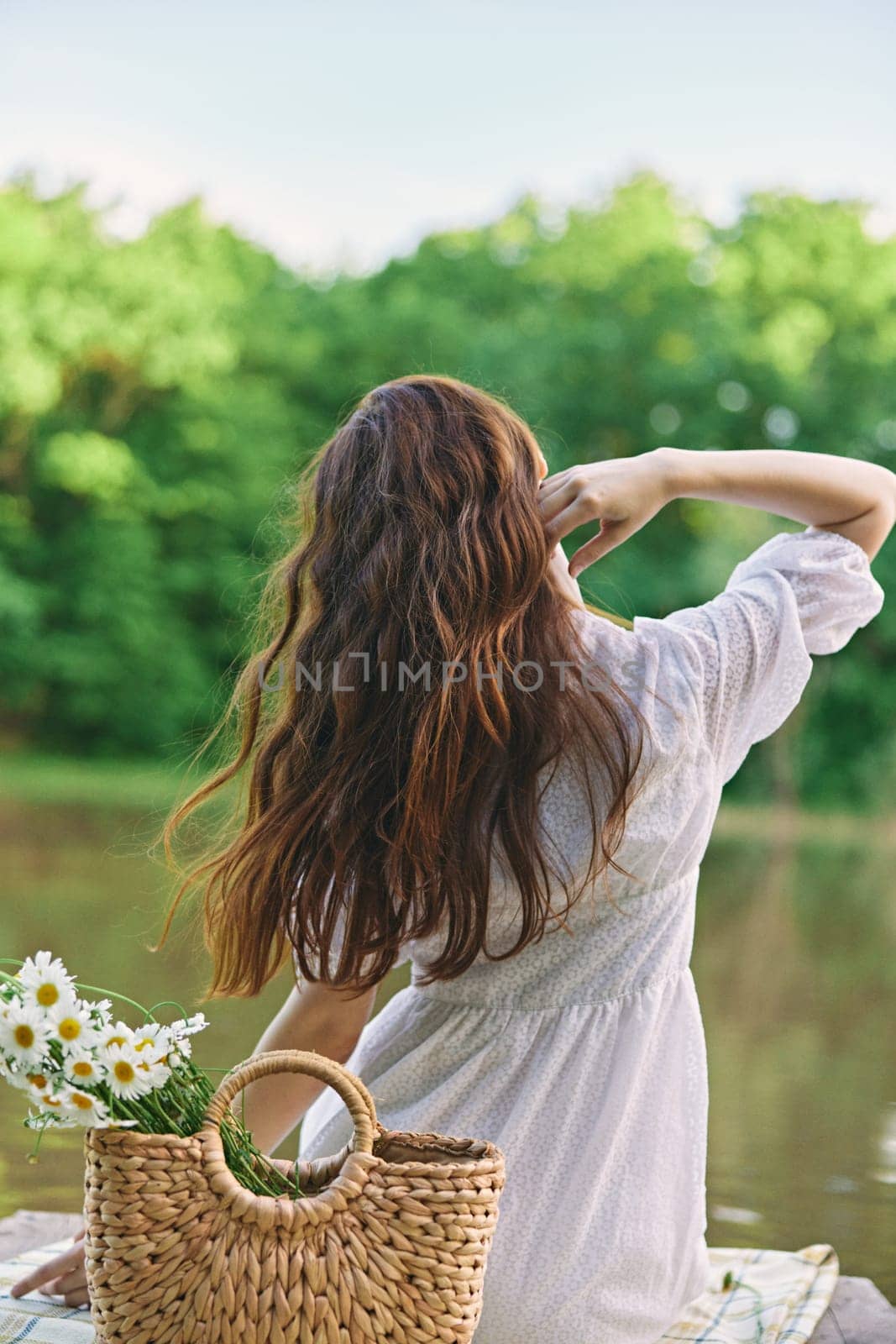 a woman with well-groomed hair is resting on the pier sitting with her back to the camera enjoying nature by Vichizh