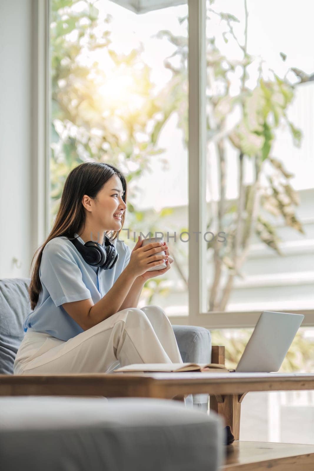 girl wearing headphones watching movies listening to music on laptop on the sofa at home on vacation with a cup of coffee..