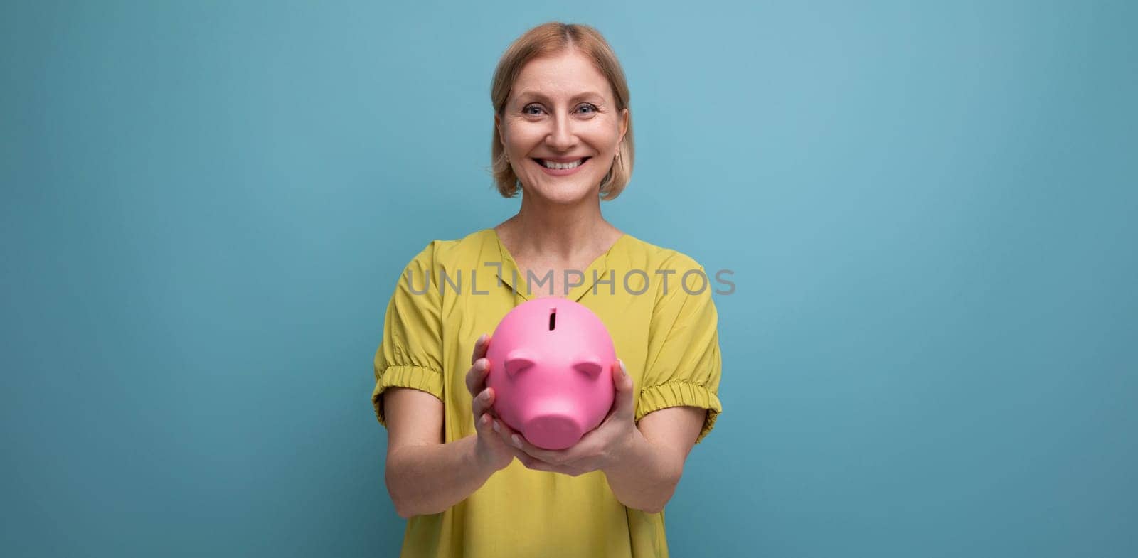 successful blonde mature woman keeps money in a piggy bank and thinks where to invest it.