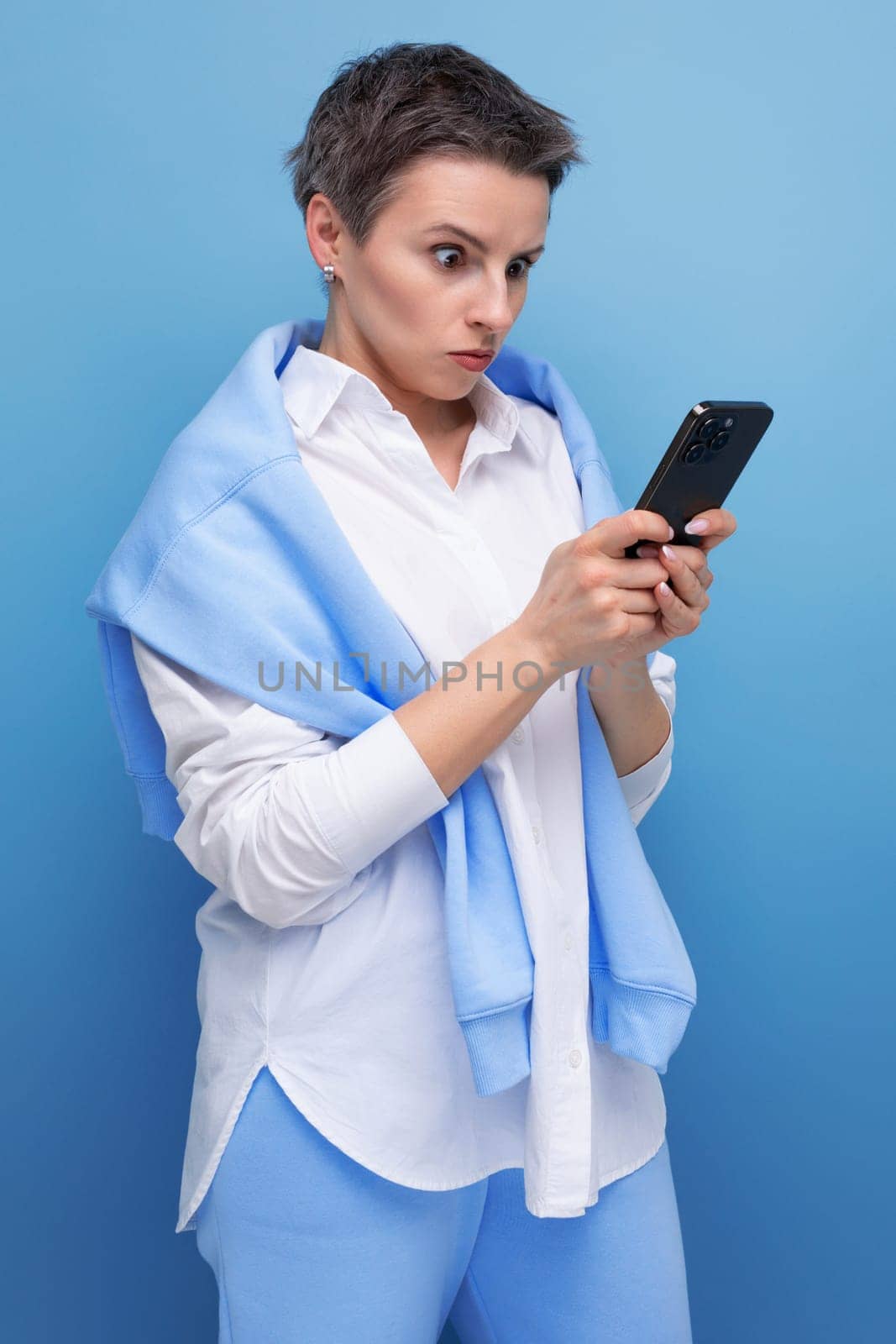 concentrated young woman with short hair chatting online using smartphone.