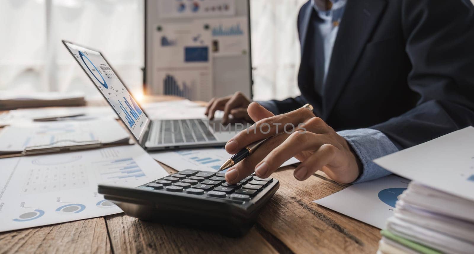 Close up Businessman using calculator and laptop for do math finance on wooden desk in office and business working background, tax, accounting, statistics and analytic research concept...