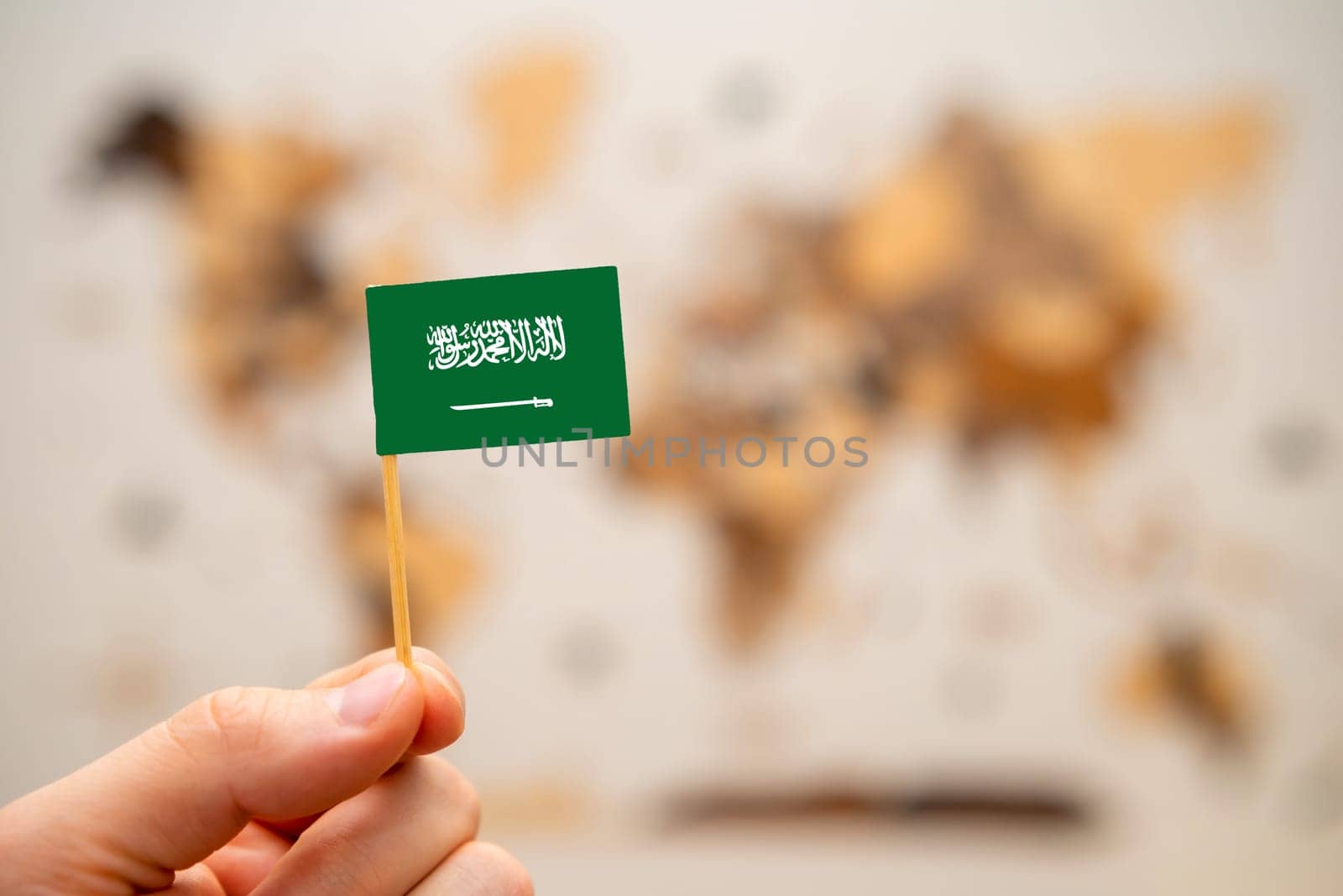 Saudi Arabia flag in mans hand on the world map background. by vladimka