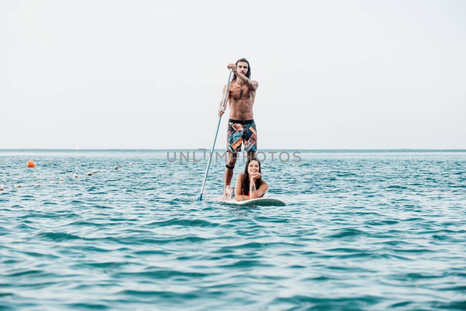 Silhouette of woman standing, surfing on SUP board, confident paddling through water surface. Idyllic sunset or sunrise. Sports active lifestyle at sea or river.