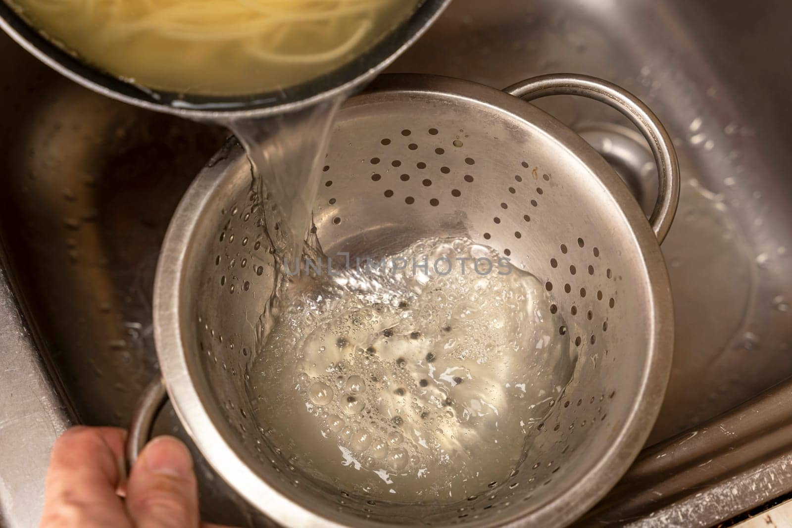 Colander with fresh cooked spaghetti. Woman pouring water from boiled spaghetti into colander. Spaghetti being poured into a colander. Pouring of water from boiled pasta over a kitchen sink.