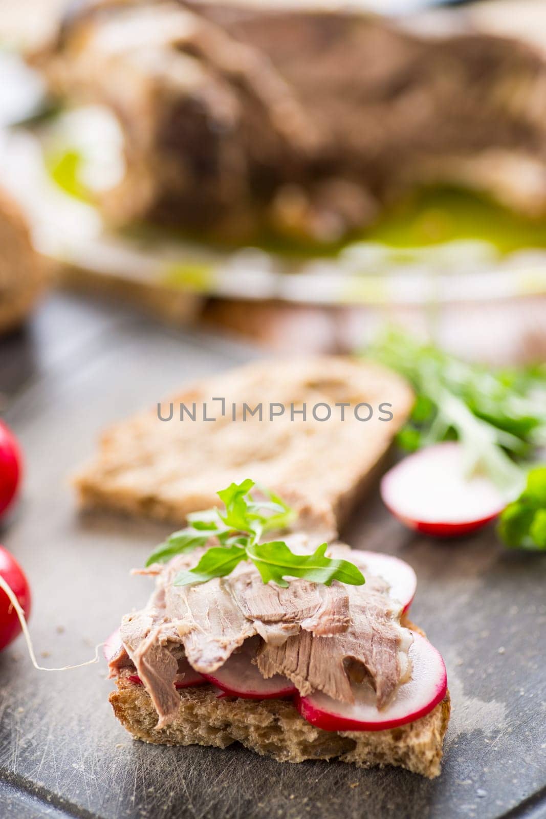 sandwich with baked meat, radish and herbs on a wooden table.