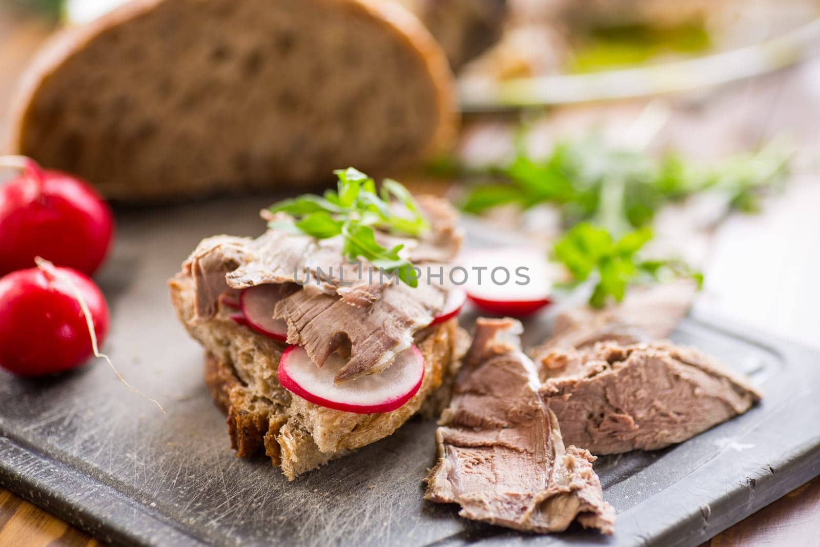 sandwich with baked meat, radish and herbs on a wooden table.