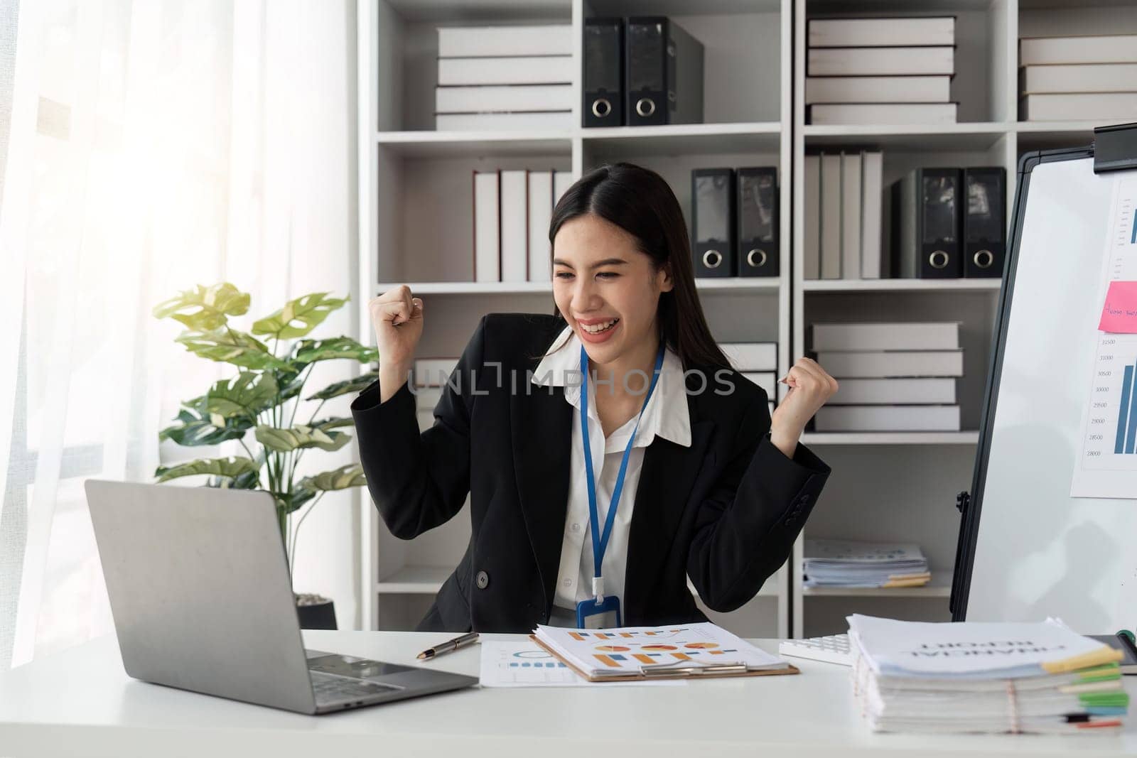 business asian woman triumphing in office happy excited successful Portrait of a cheerful Asian businesswoman sitting at the table in office by nateemee