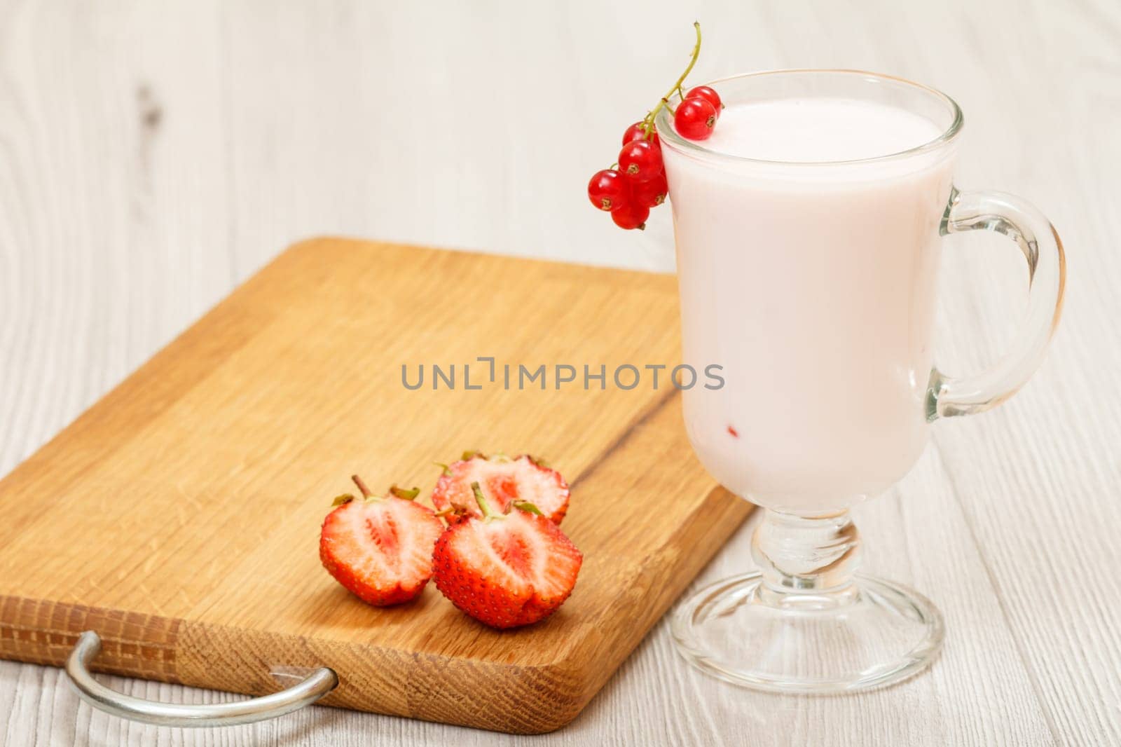 Glass of delicious strawberry yogurt with mint leaves and fresh strawberries on wooden cutting board.