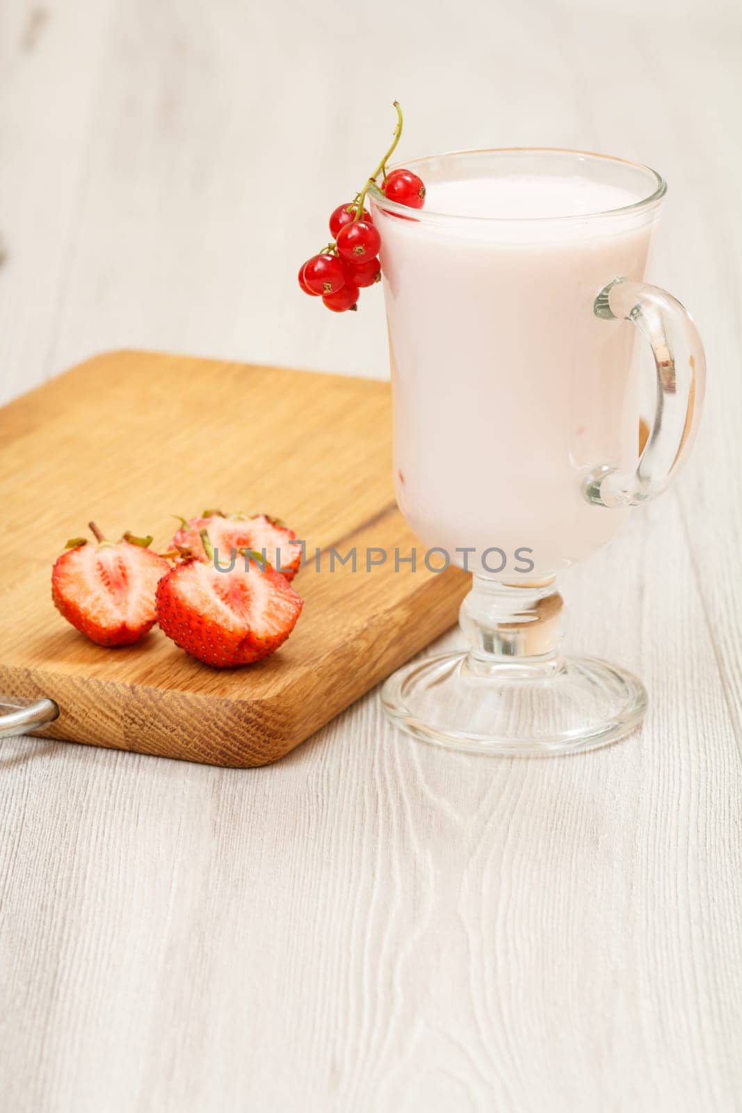 Glass of delicious strawberry yogurt with mint leaves and fresh strawberries on wooden cutting board.