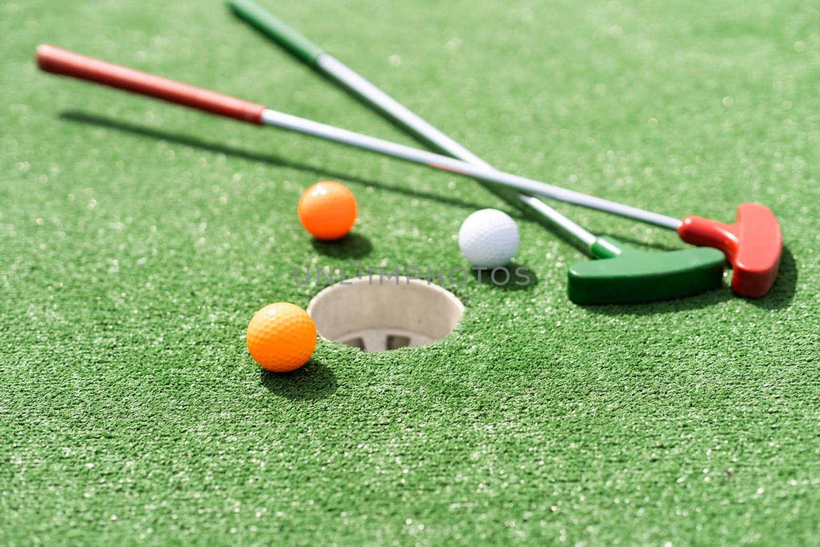 Close-up of miniature golf hole with bat and ball.