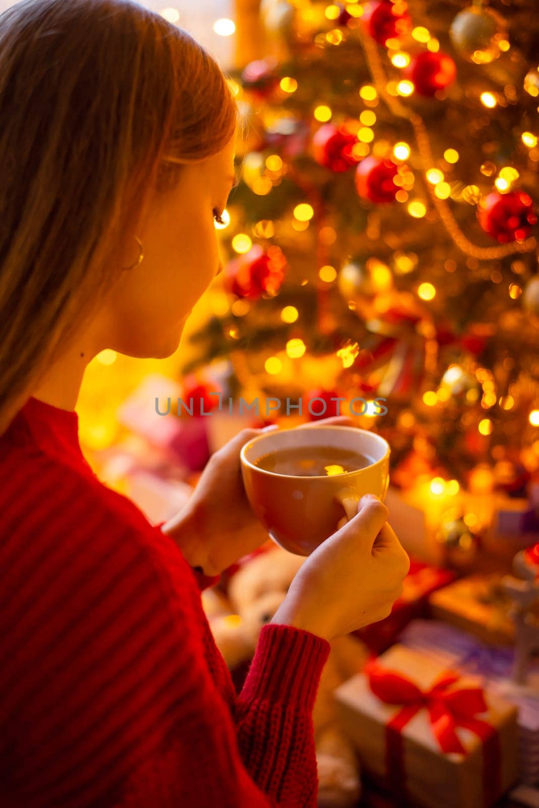 Young girl drinking tea and relaxing near the Christmas tree
