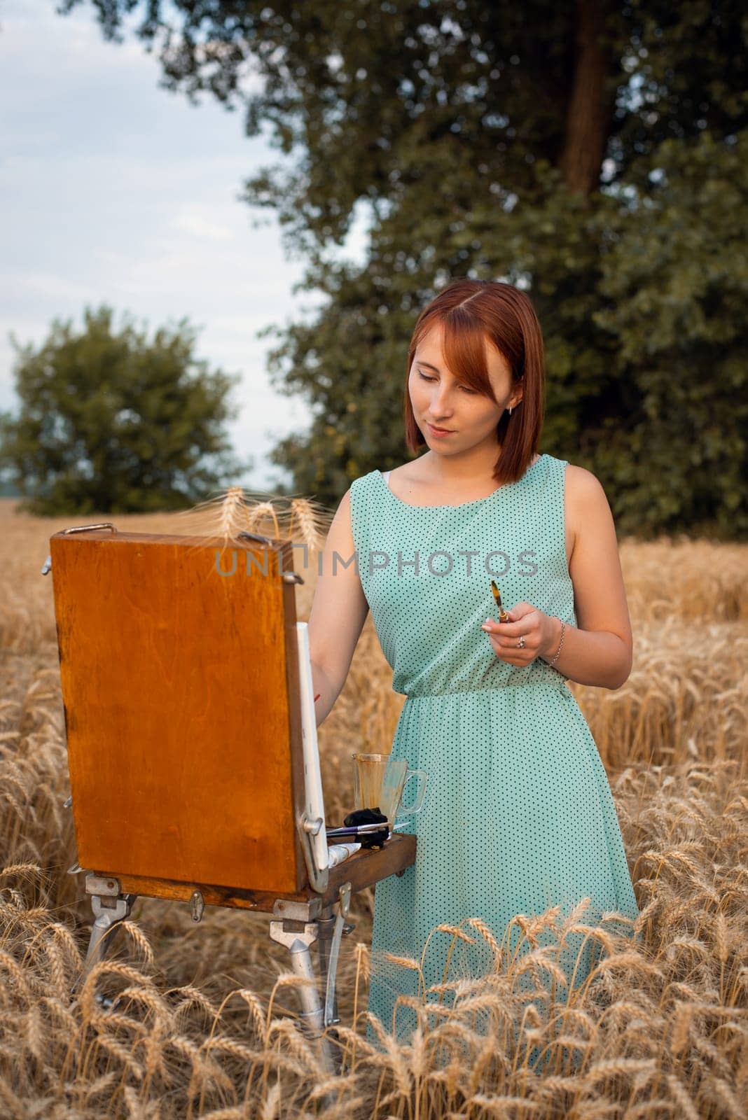 Red-headed girl artist creates work of art in the field on a warm summer day
