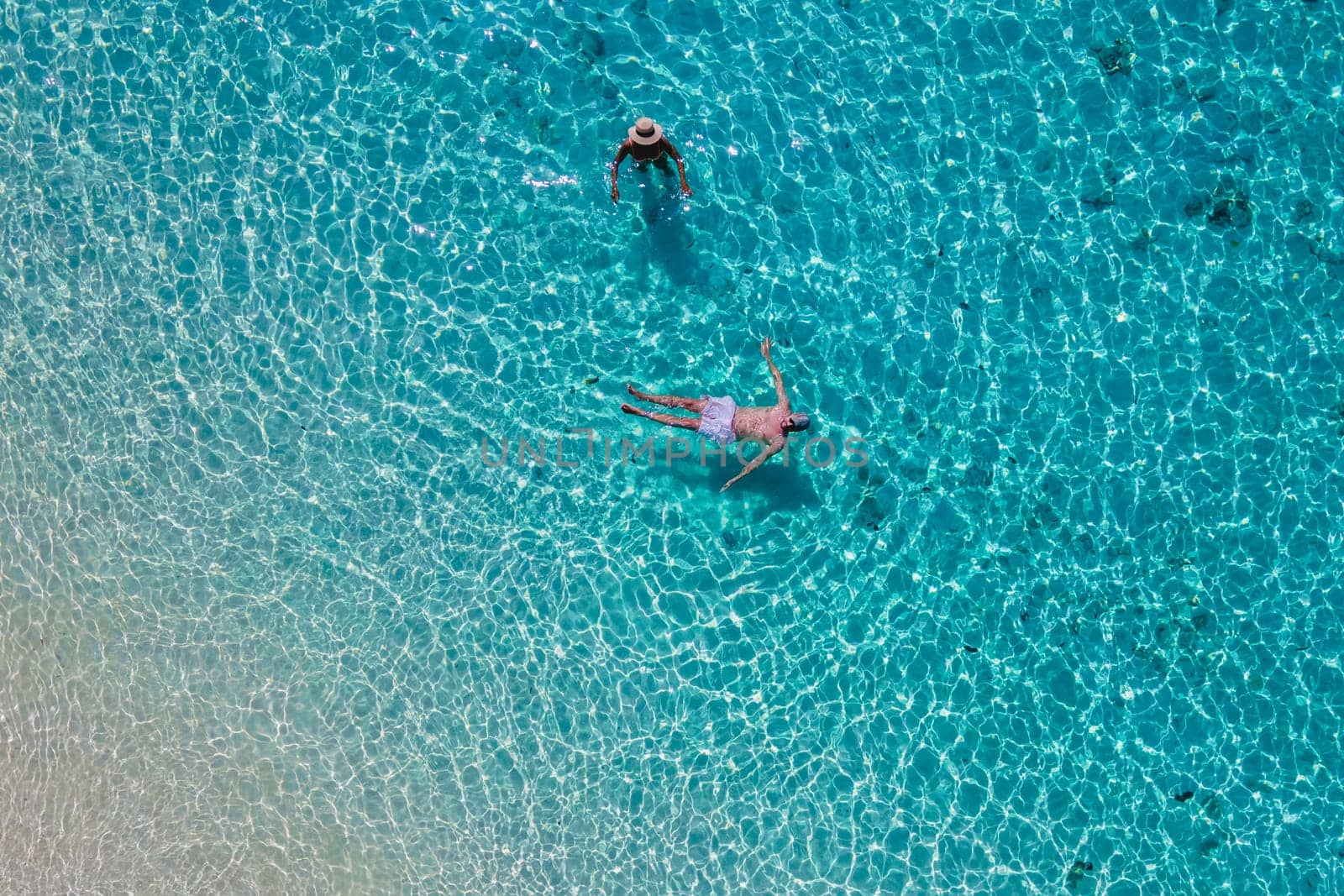 a couple swimming in the ocean of Koh Kradan Island with a white tropical beach and turqouse colored ocean. men and women in a blue ocean seen from above with a drone