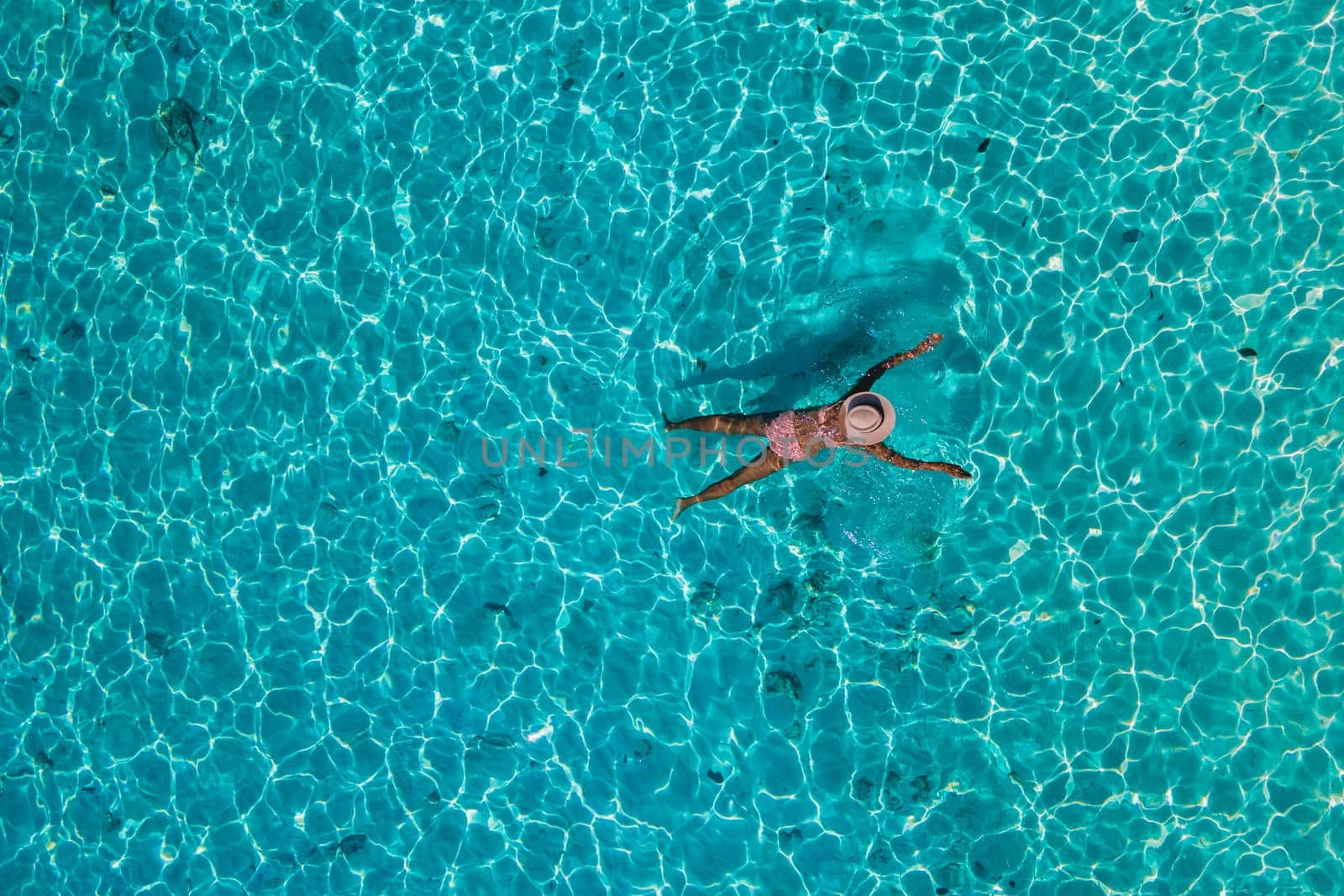 women swimming in the ocean of Koh Kradan Island with a white tropical beach and turqouse colored ocean. women in blue ocean seen from above with a drone