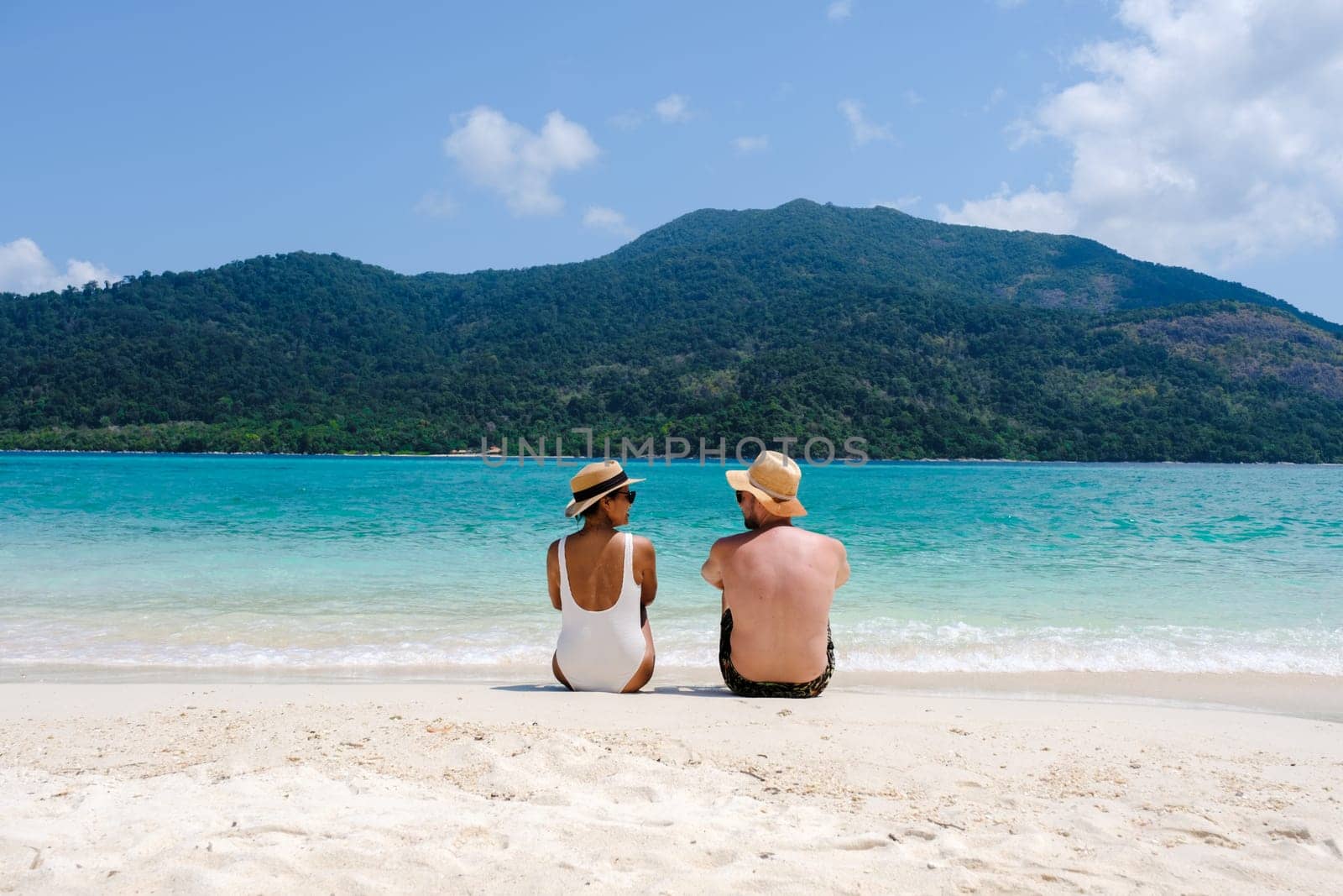 Couple on the beach of Koh Lipe Island Thailand, a tropical Island with a blue ocean and white soft sand. Ko Lipe Island Thailand. men and women relaxing on the beach looking out over ocean