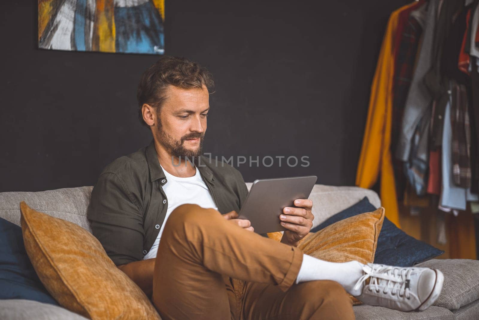 Happy man home, focused on tablet PC. Emphasis is on digital device, representing ubiquity of technology in modern life. Man's positive and upbeat demeanor reflects sense of joy and satisfaction, conveying the importance of taking breaks and enjoying leisure time. High quality photo