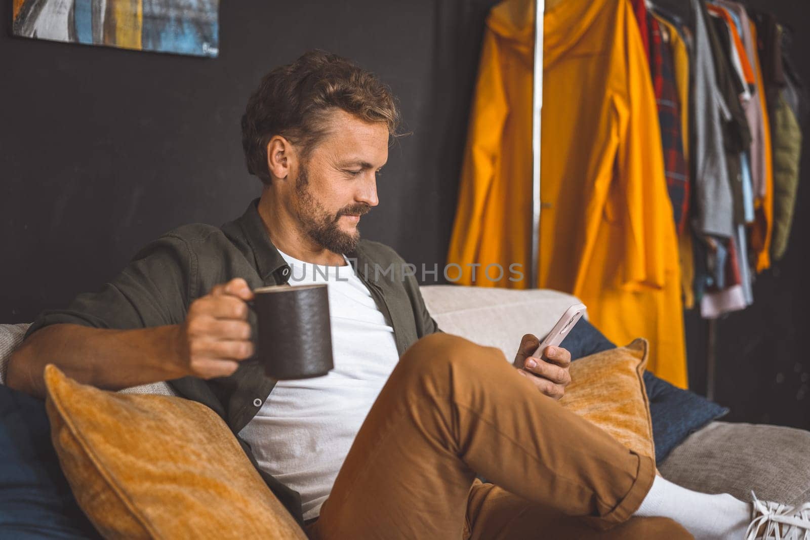 Man taking break at home, enjoying cup of coffee while focused on phone. Concept of spending time at home is emphasized, highlighting the importance of relaxation and leisure in our daily routines. High quality photo