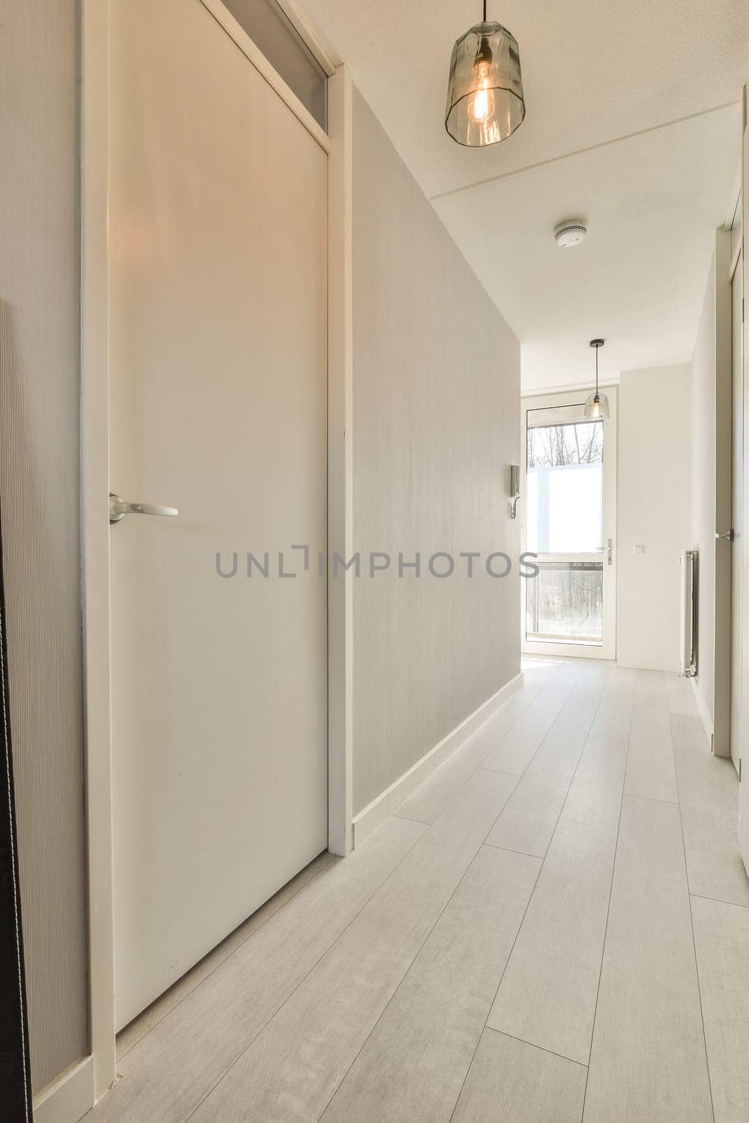 a long hallway with white walls and wood flooring on the right hand side, there is an open door leading to another room