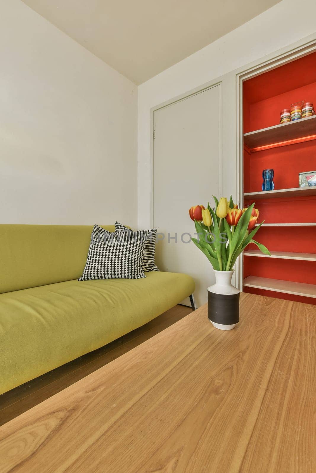 a living room with a green couch and some flowers in a white vase on the coffee table next to it