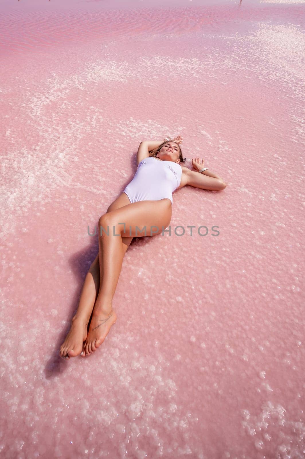 Woman in a pink salt lake. She lies in a white bathing suit. Wanderlust photo for memory by Matiunina