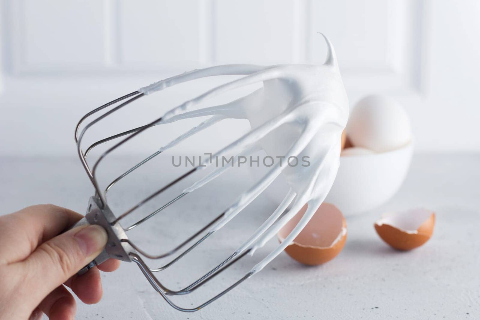 Whisked egg whites - whipped Italian meringue on a wire whisk and eggs on a gray background. copy space. by lara29