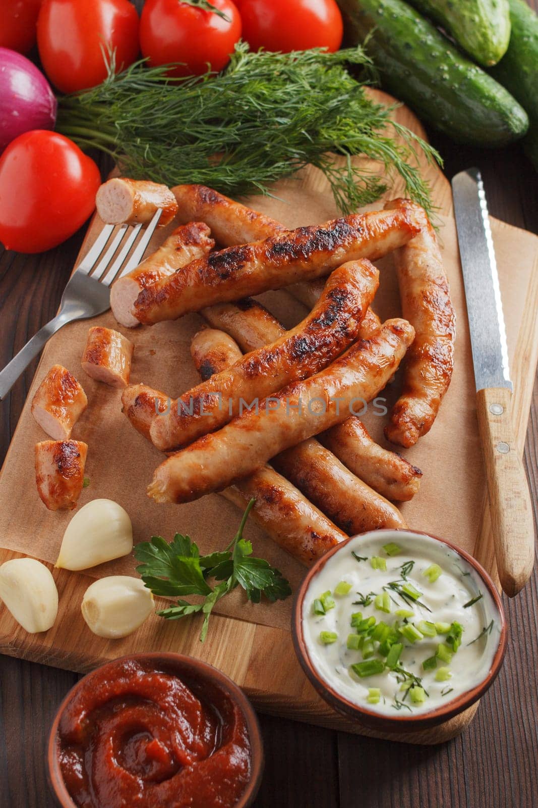 Delicious sausages on a wooden board with various sauces