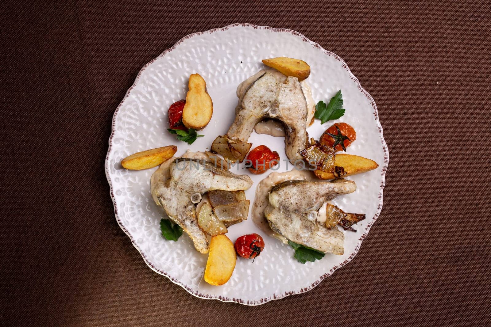 top view of the fish dish . three pieces of fish and potatoes on a plate.