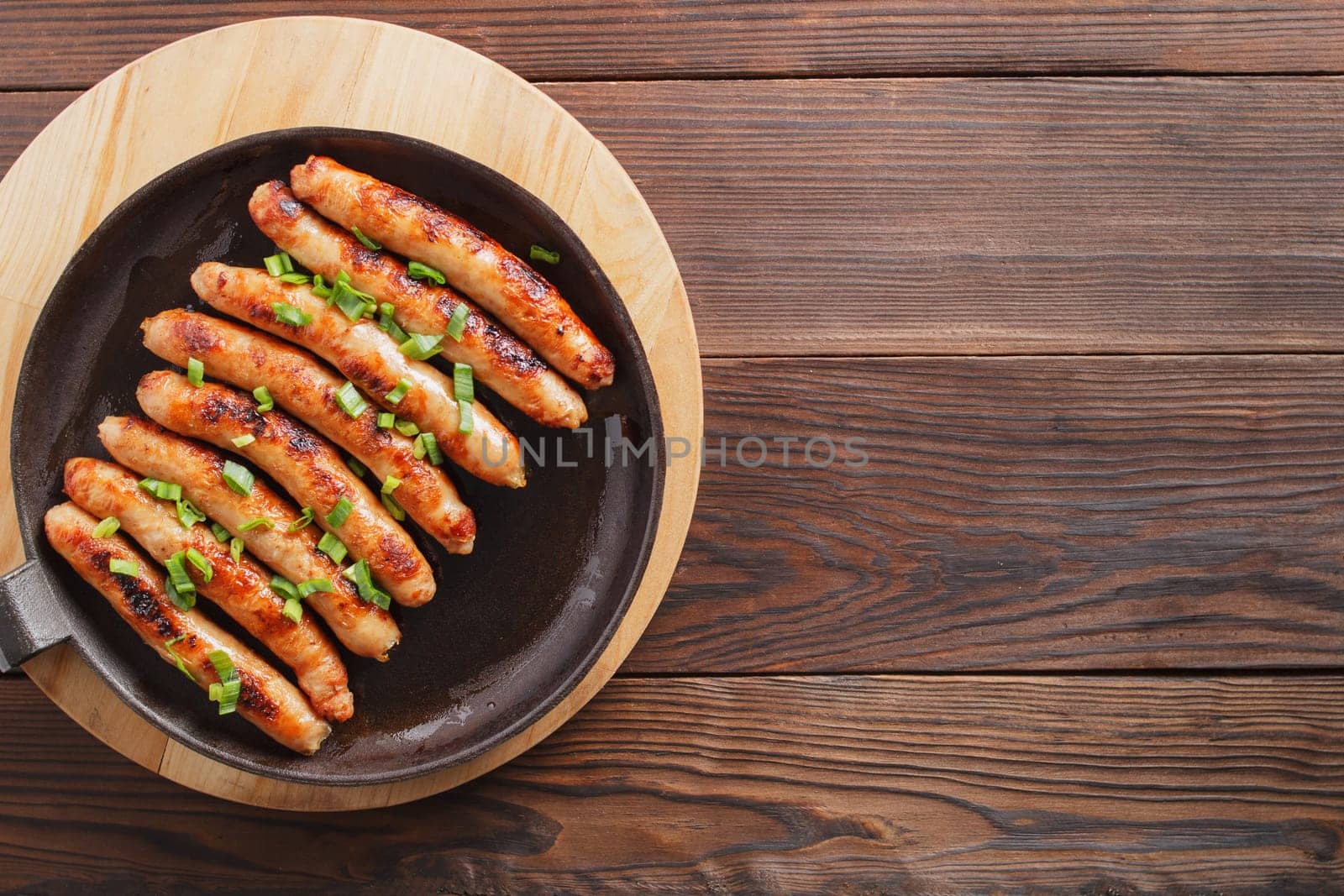 Delicious sausages cooked in a frying pan on a wooden table. copy space. by lara29