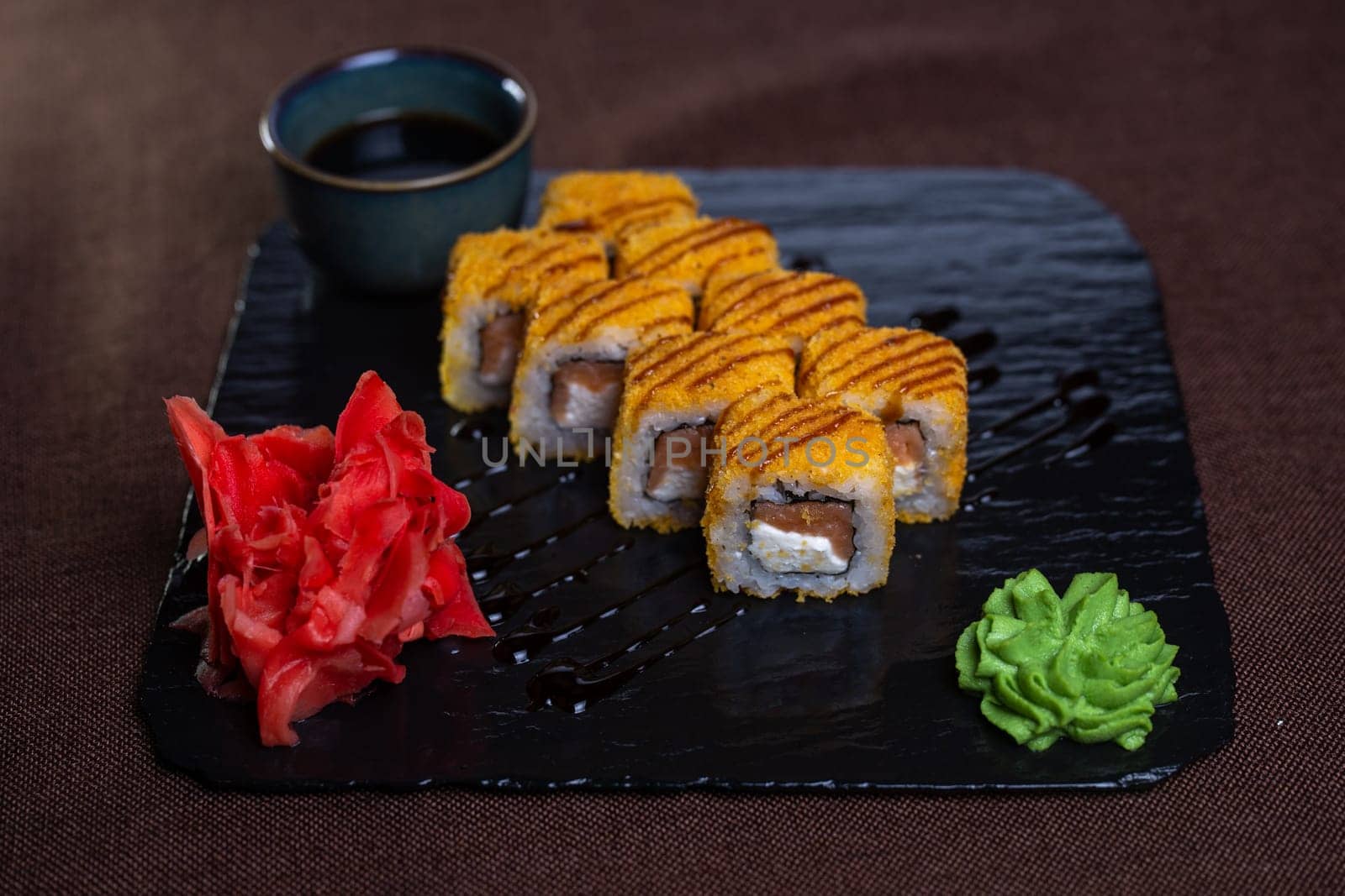 baked rolls with salmon and tender cheese with sauce on a black plate by Pukhovskiy