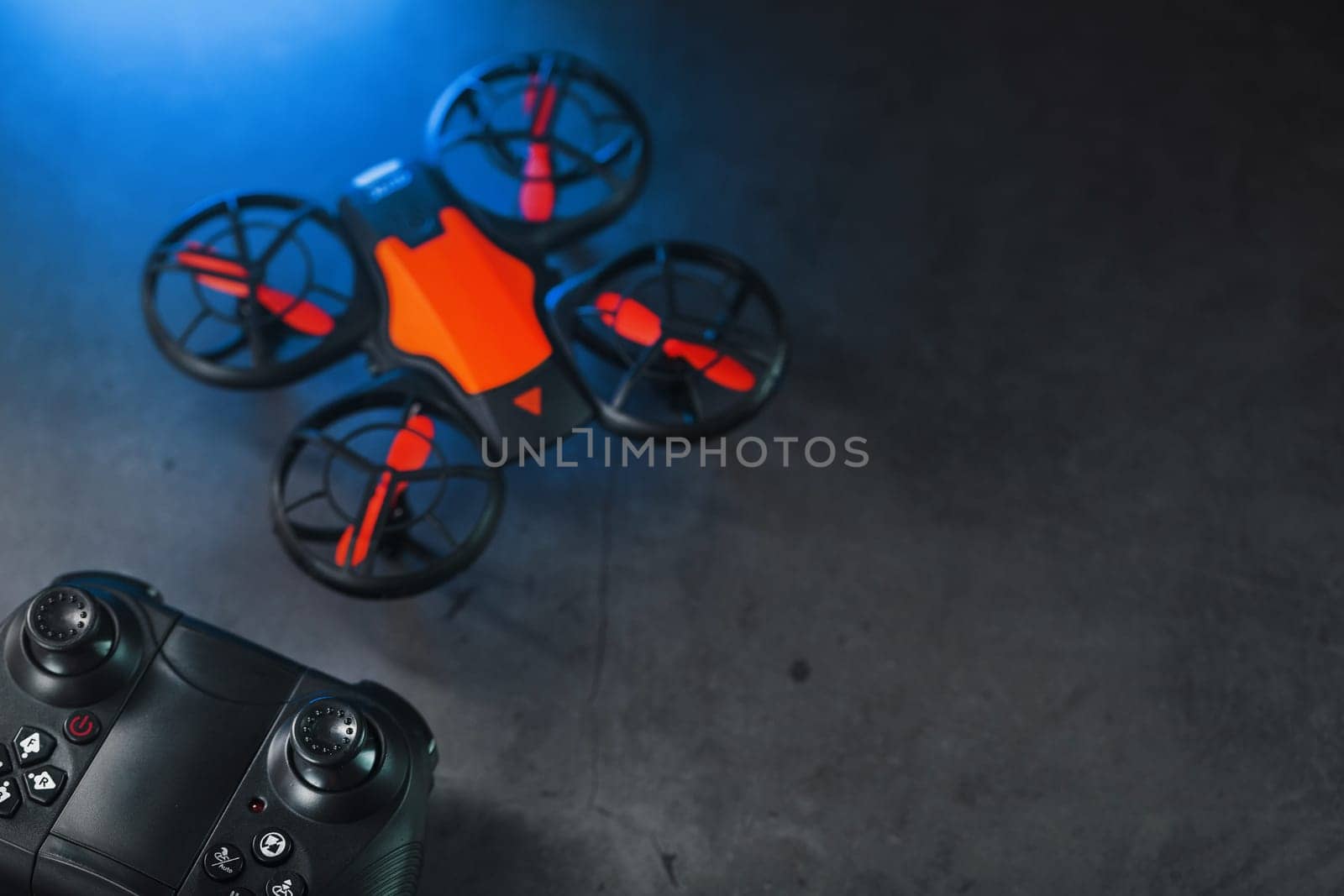 A reconnaissance quadcopter drone with an orange body and blue LED backlight on a dark background