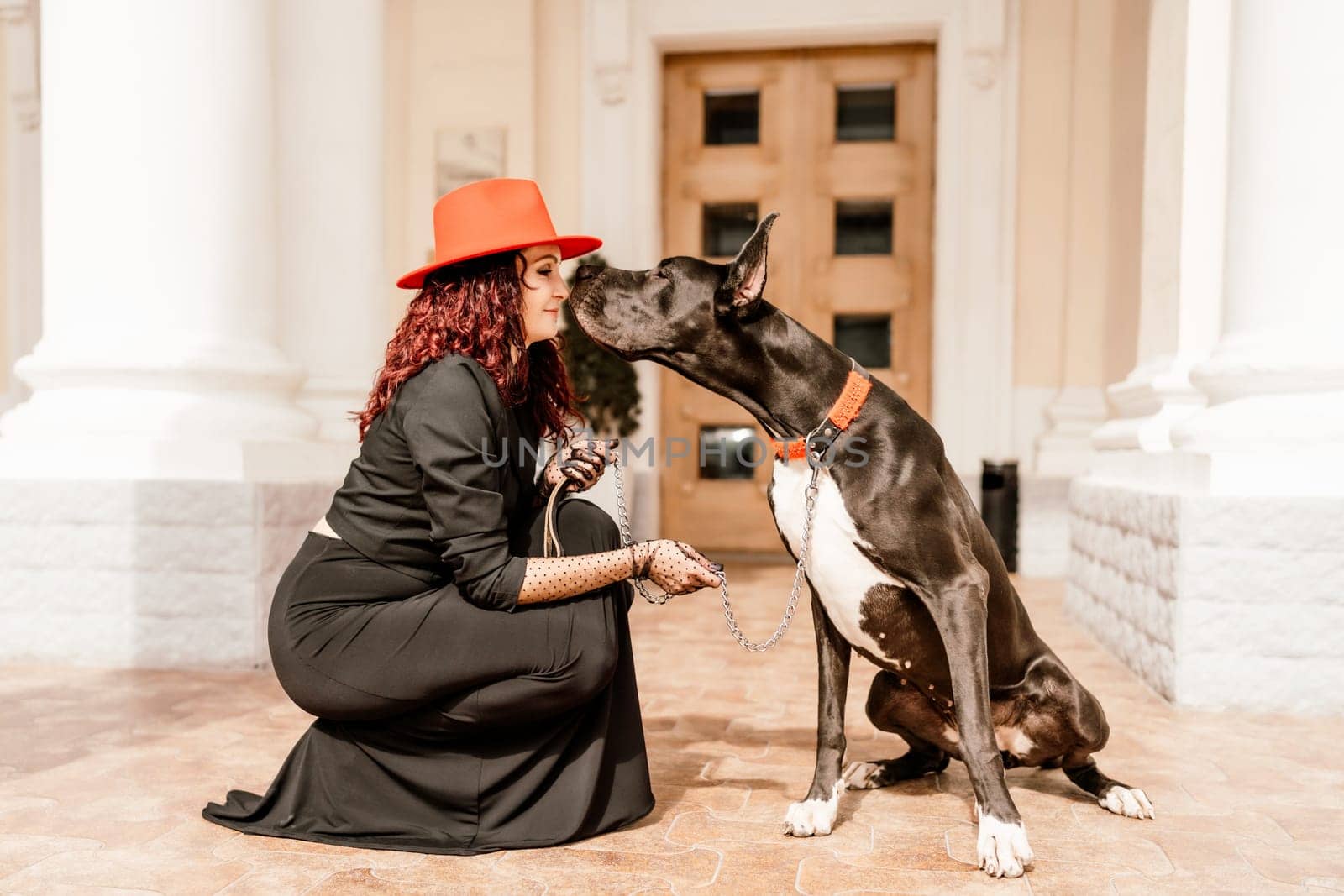 A photo of a woman and her Great Dane walking through a town, taking in the sights and sounds of the urban environment.