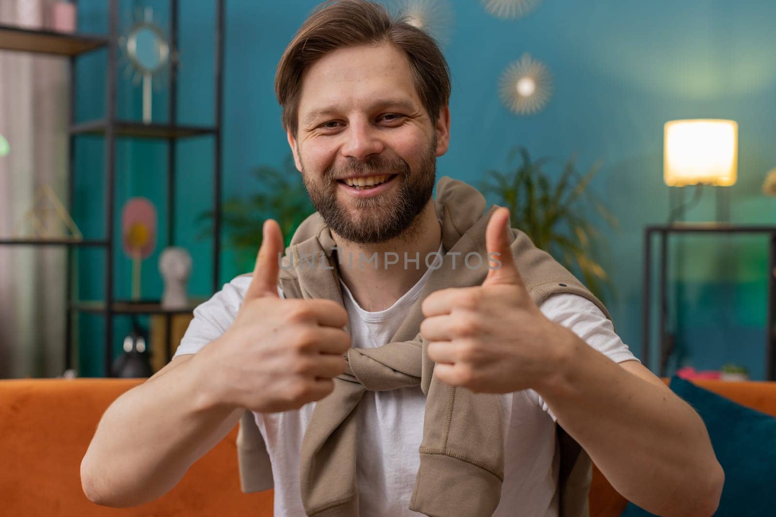 Like. Happy excited Caucasian man looking approvingly at camera showing thumbs up, like sign positive something, good great news, positive feedback. Young guy sitting on couch at home living room