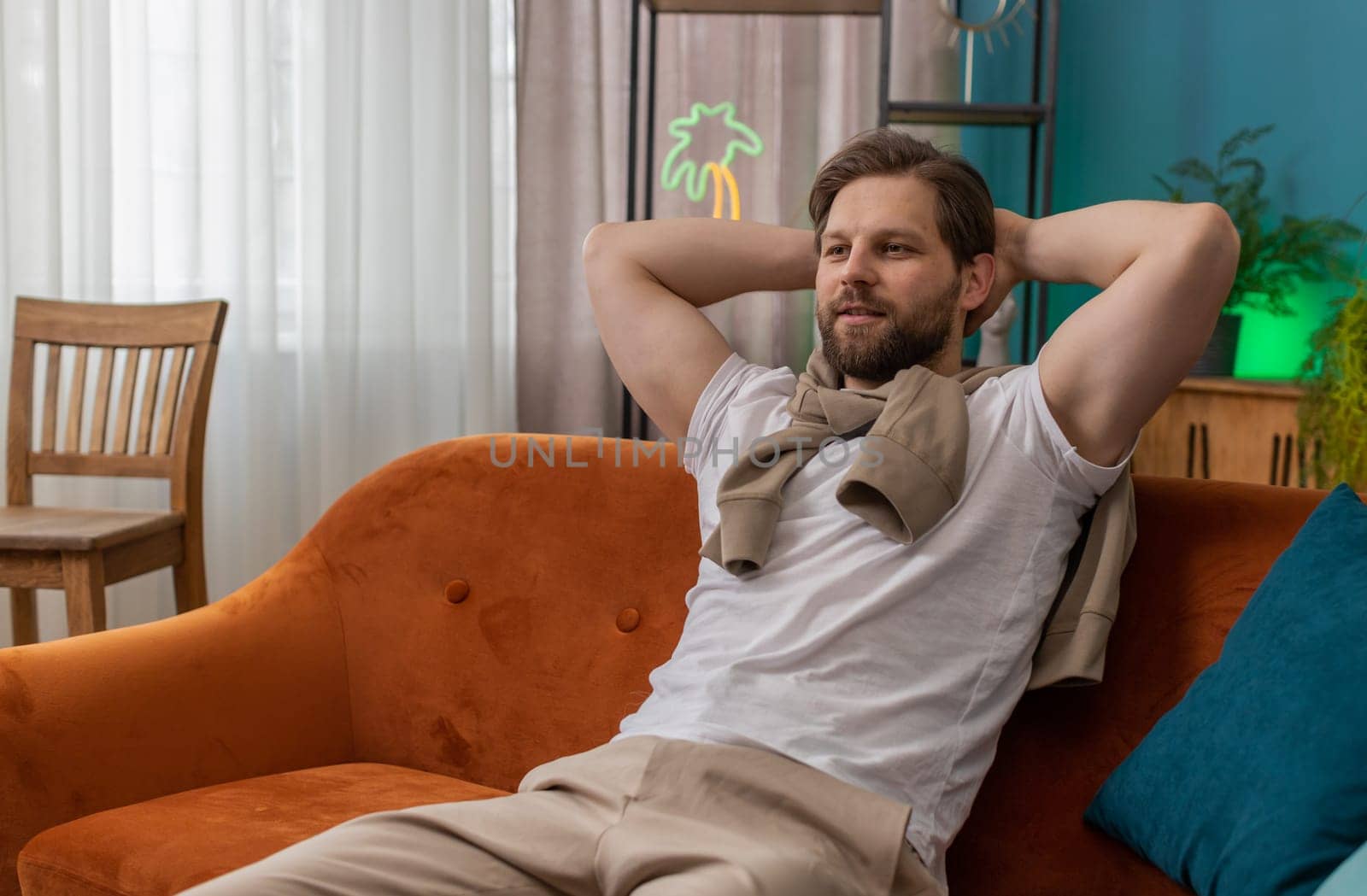 Tired man lying down on comfortable couch, taking a rest, daytime nap. Portrait of carefree Caucasian guy holding hands behind head relaxing, falling asleep at home apartment living room on sofa