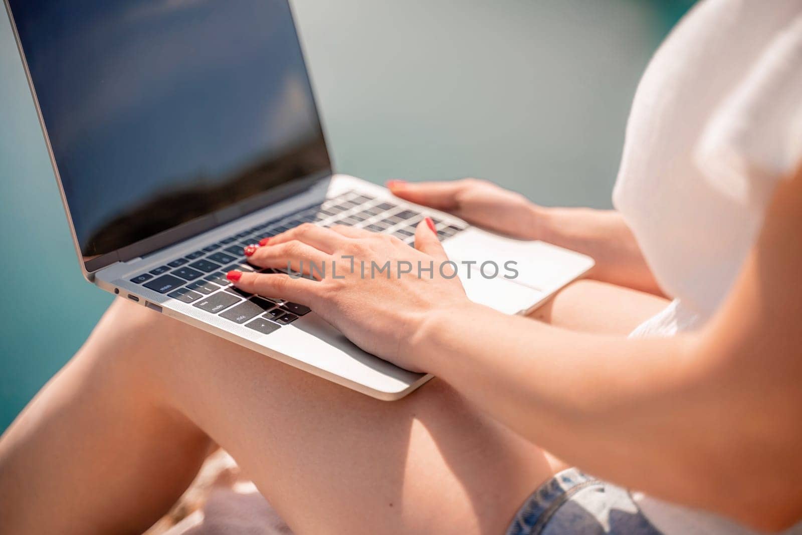 Freelance women sea working on the computer. Good looking middle aged woman typing on a laptop keyboard outdoors with a beautiful sea view. The concept of remote work. by Matiunina