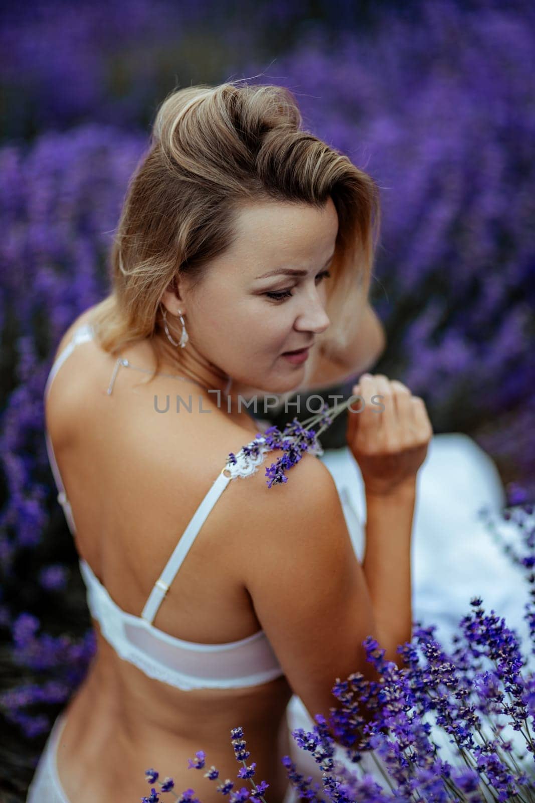 A middle-aged woman sits in a lavender field and enjoys aromatherapy. Aromatherapy concept, lavender oil, photo session in lavender by Matiunina