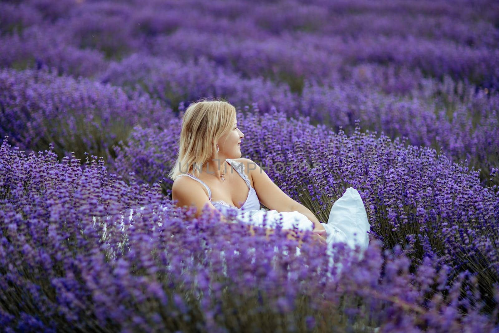 A middle-aged woman sits in a lavender field and enjoys aromatherapy. Aromatherapy concept, lavender oil, photo session in lavender.