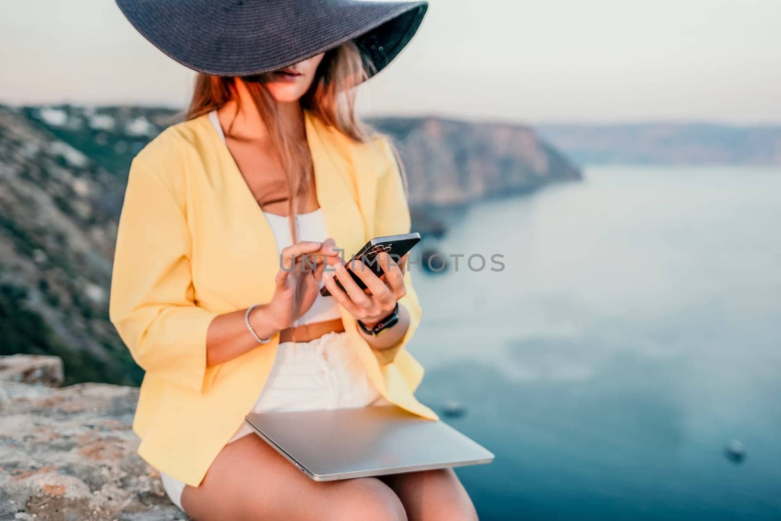 Digital nomad, Business woman working on laptop by the sea. Pretty lady typing on computer by the sea at sunset, makes a business transaction online from a distance. Freelance, remote work on vacation by panophotograph