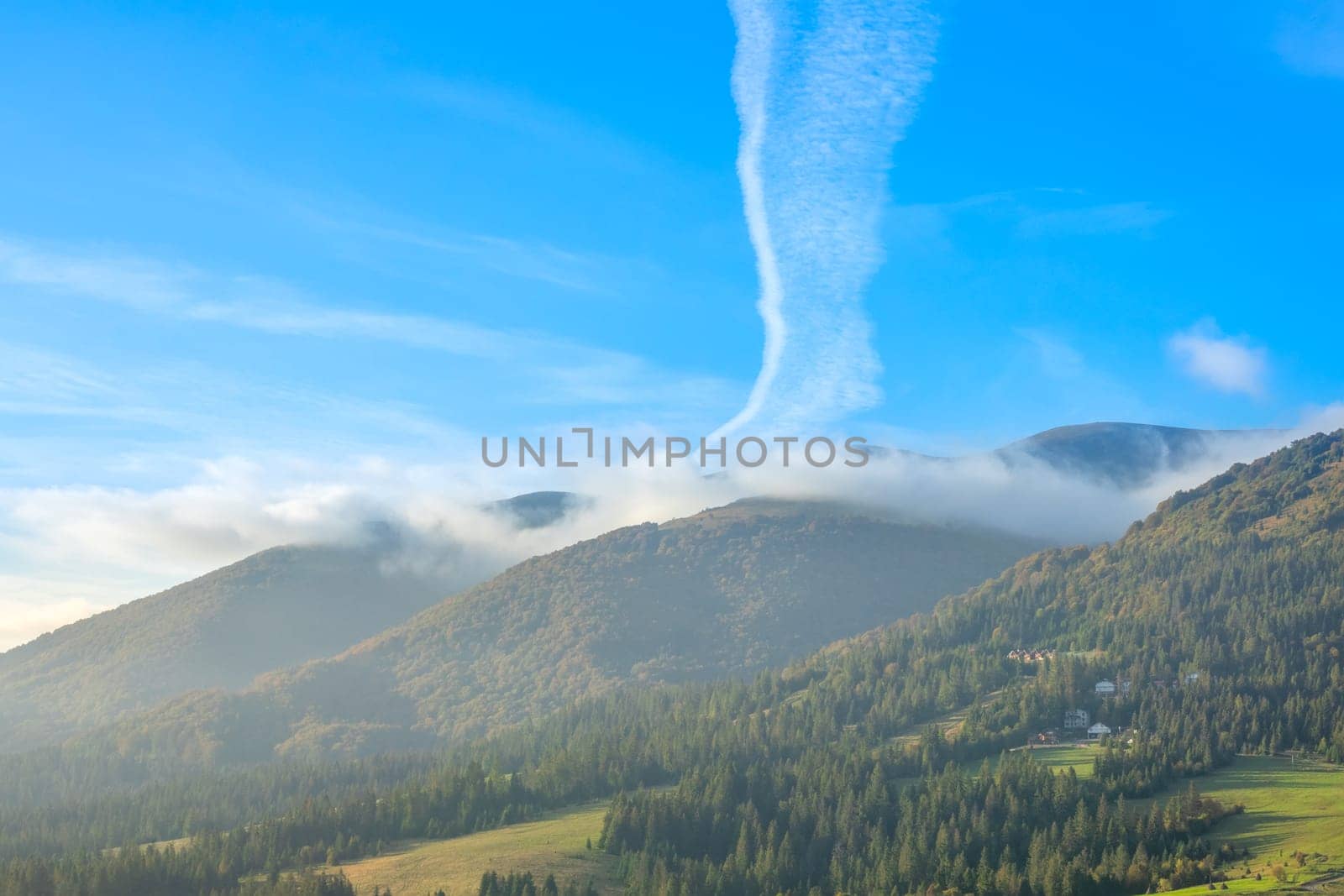 Sunny summer morning in the Ukrainian Carpathians. Slight fog and clouds over wooded mountains