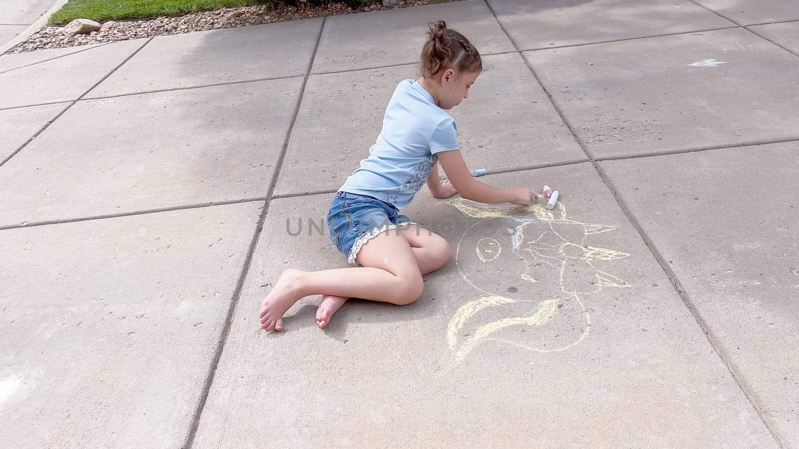 Little girl drawing chalk art on a suburban driveway on a summer day.