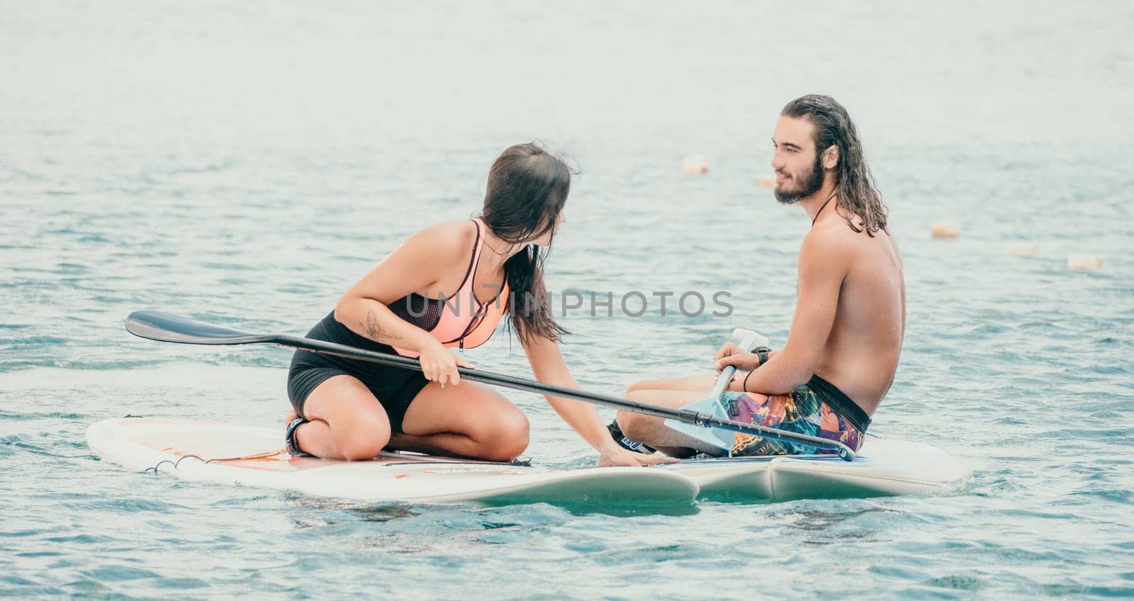 Sea woman and man on sup. Silhouette of happy young woman and man, surfing on SUP board, confident paddling through water surface. Idyllic sunset. Active lifestyle at sea or river